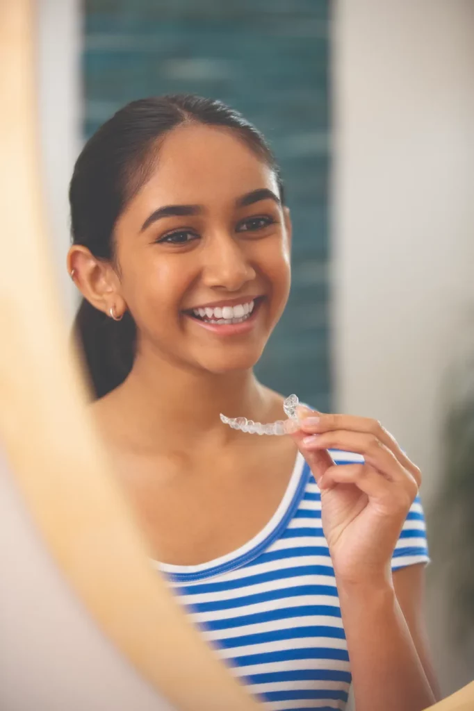 woman smiling in mirror holding her Invisalign